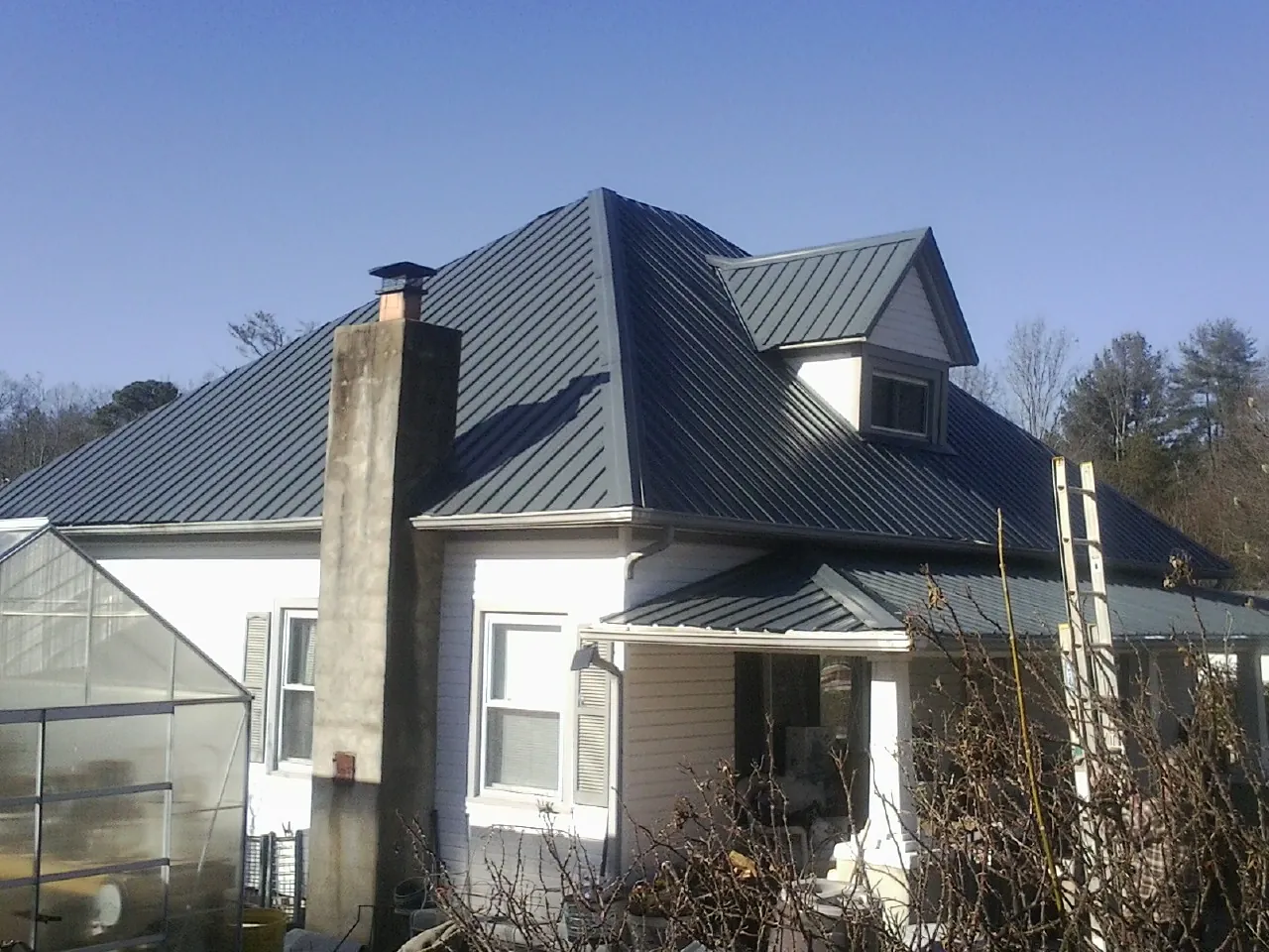 Dark blue standing seam metal roof on a white farmhouse with dormer — Slate & Tile Roof Repair by Roofing Brothers in Elmore City