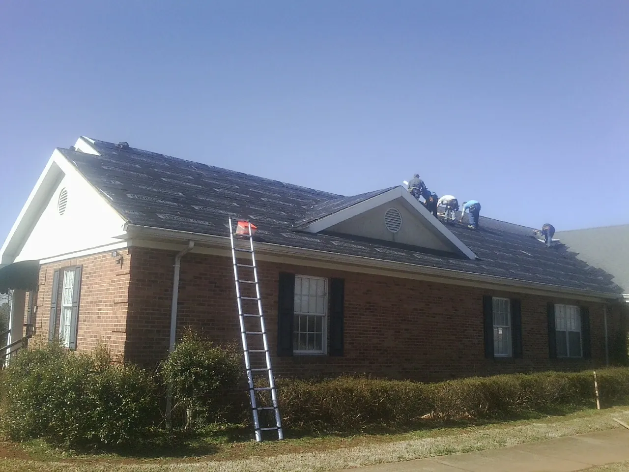 Crew tearing shingles off a brick ranch roof with a ladder set — Metal Roof Repair work by our crew in Elmore City