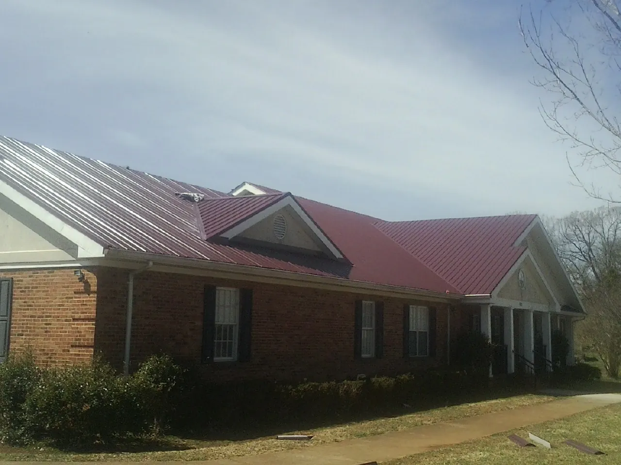 Red metal roof with gabled entries on a long brick building, from a Hail Damage Roof Repair job in Elmore City