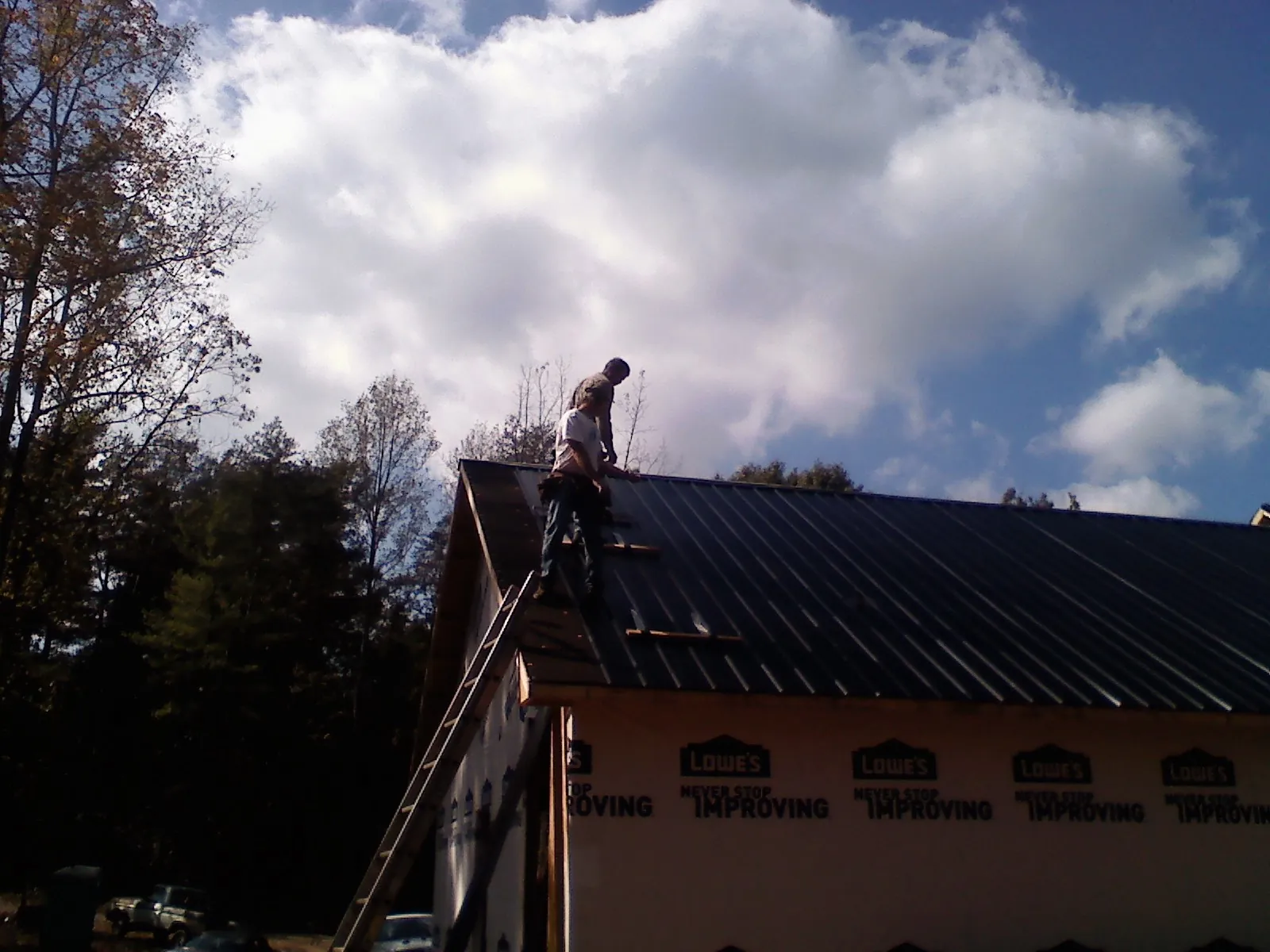 Roofer fastening dark metal panels high against a cloudy sky, from a Roof Inspection job in Elmore City