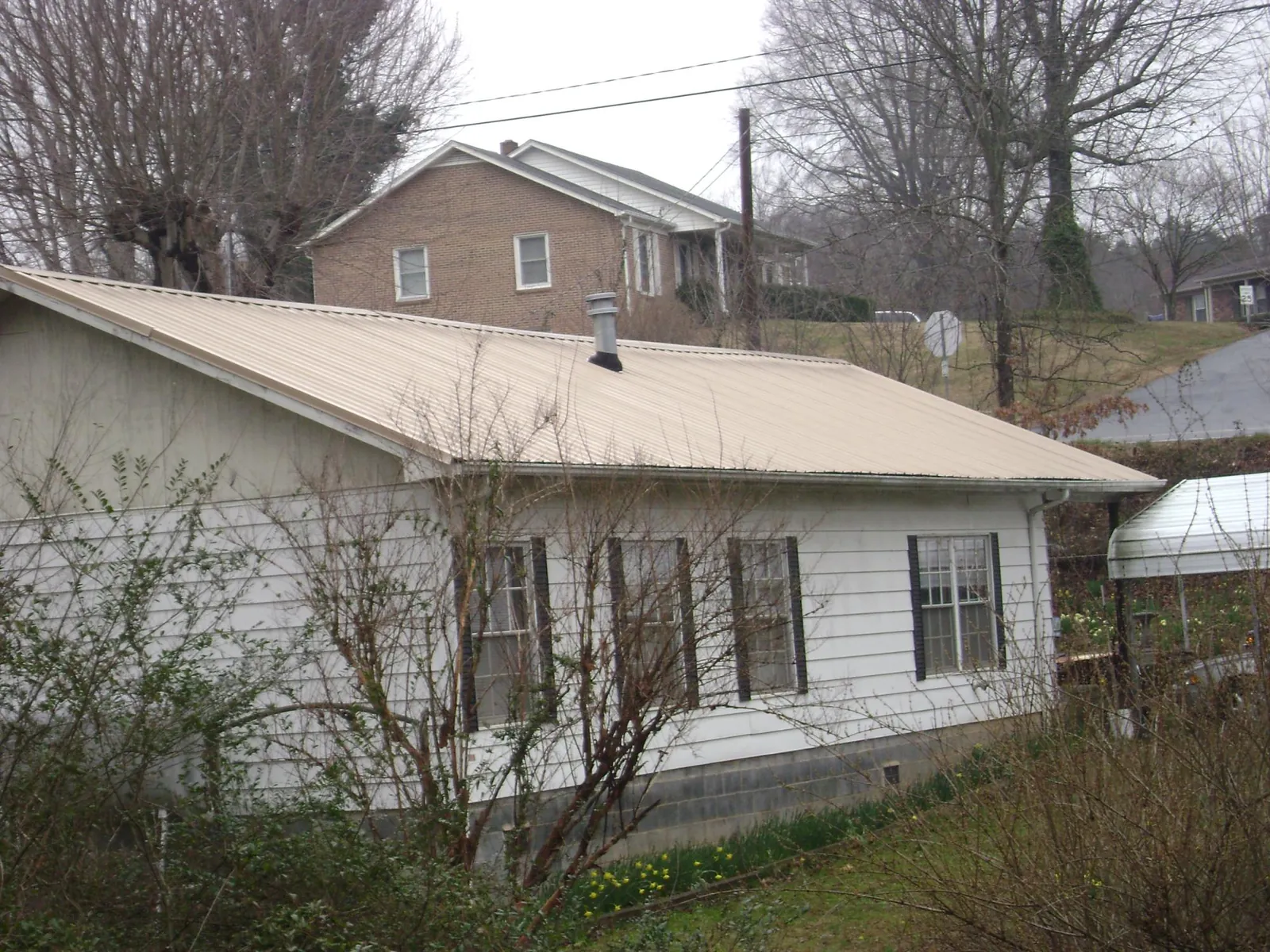 Tan metal roof on a white sided house set into a hillside — Commercial Roofing by Roofing Brothers in Elmore City