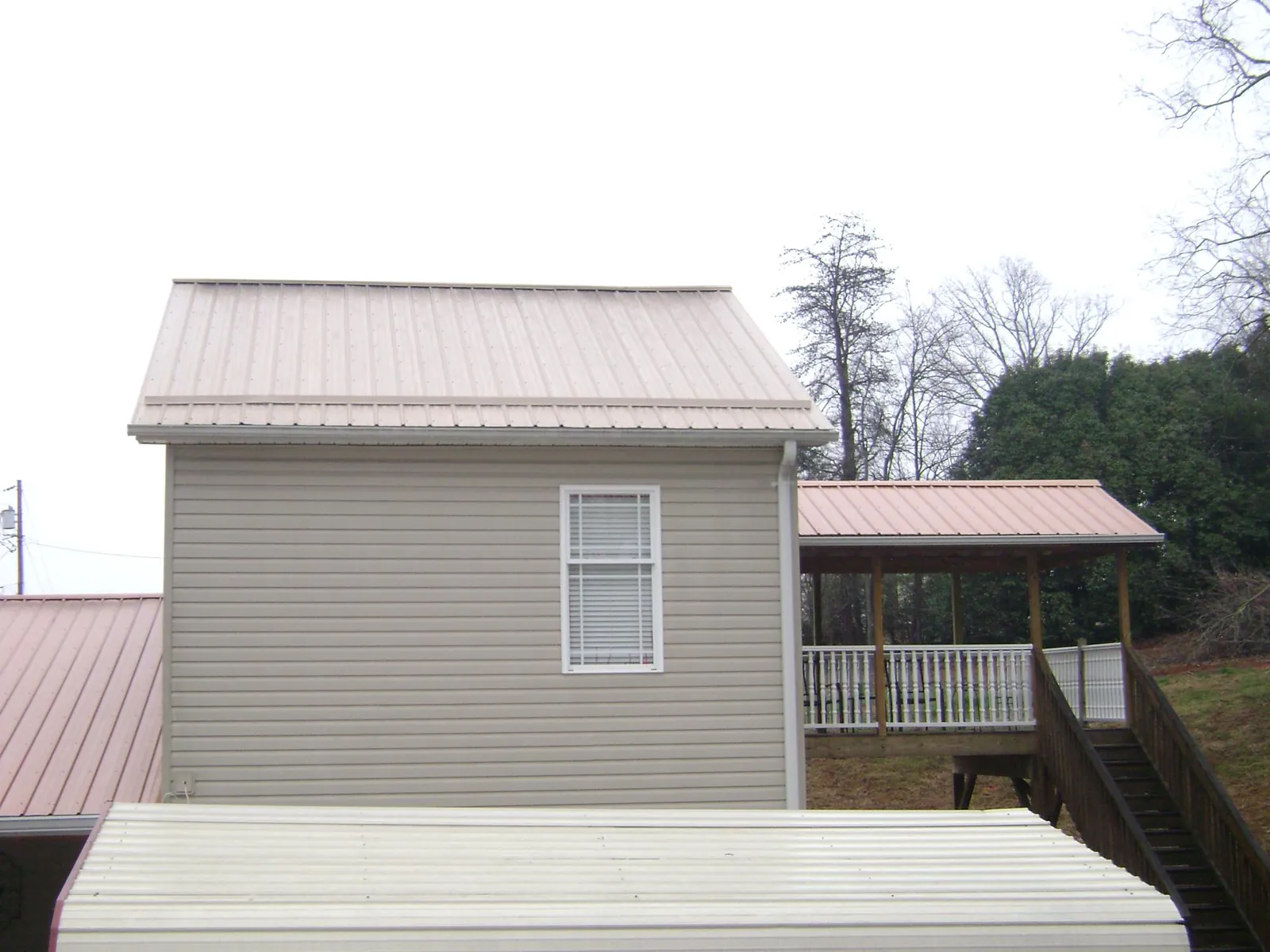 Tan metal roofs on a two story addition and attached porch, from a Roof Replacement job in Elmore City