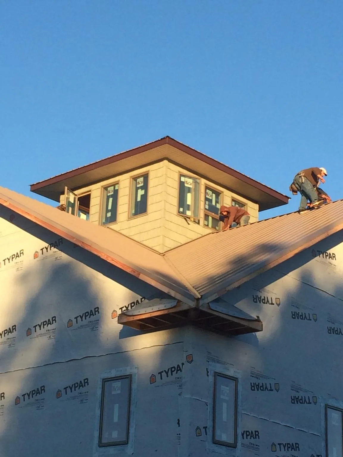 Roofers working around a rooftop cupola on a new metal roof at sunset — Roof Waterproofing in Elmore City by Roofing Brothers